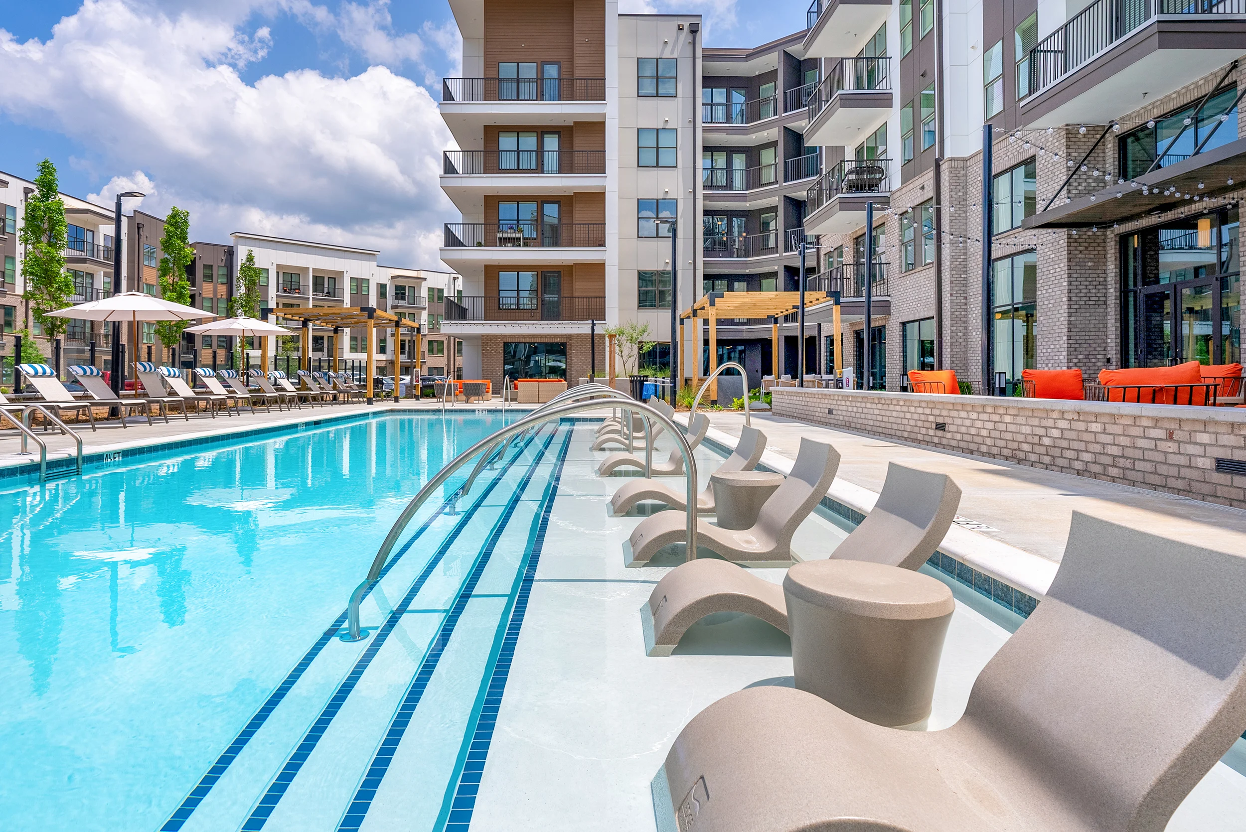 Modern Apartment Pool Area A luxurious outdoor swimming pool with modern lounge chairs lined up along one side, surrounded by contemporary apartment buildings and landscaped areas.