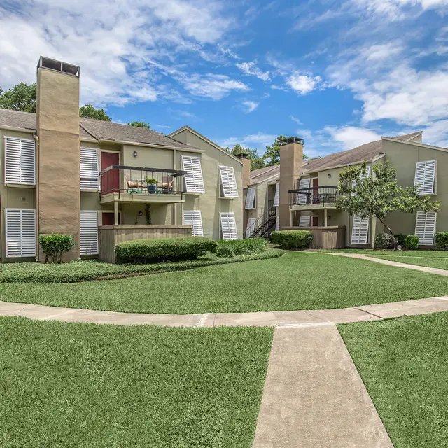 A well-maintained apartment complex surrounded by neatly trimmed grass, featuring two-story buildings with balconies and lush greenery.