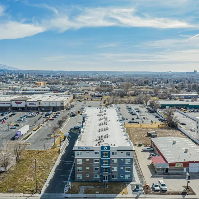 Aerial view of a cityscape with a mix of commercial buildings and parking lots, mountains visible in the background.