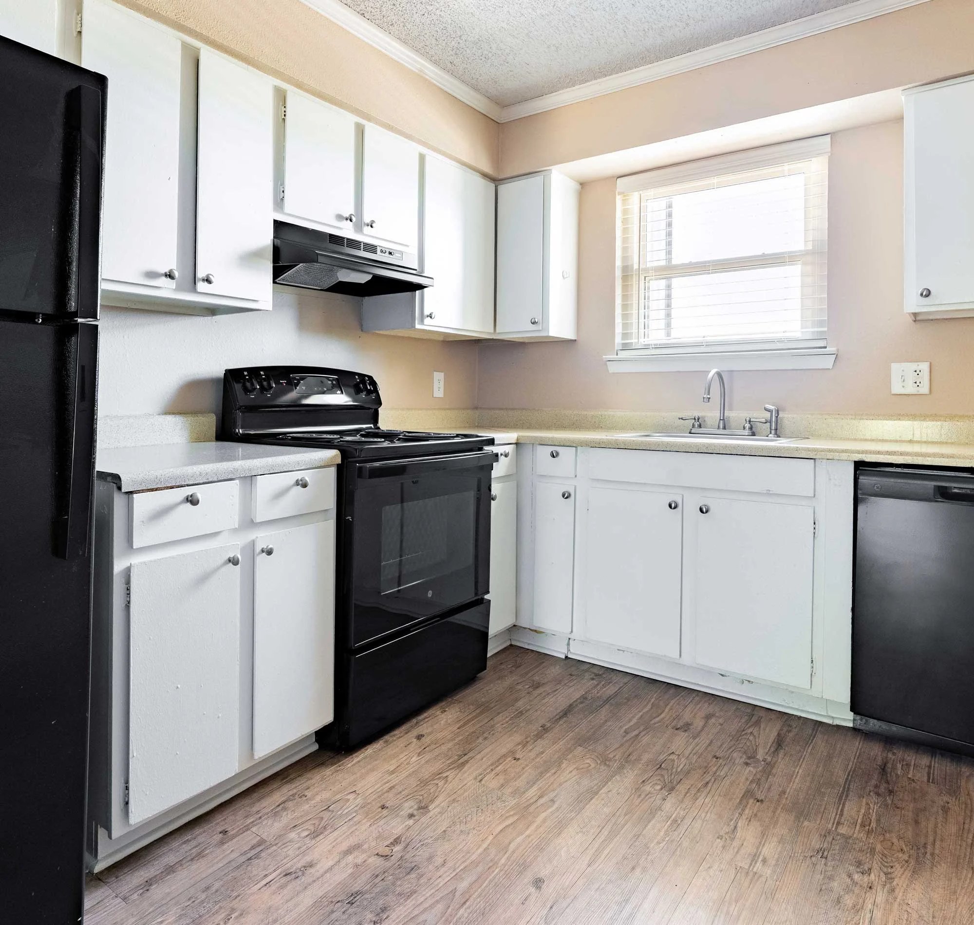 A modern kitchen featuring black appliances, white cabinets, and dark wood flooring. The room has ample natural light coming through a window.