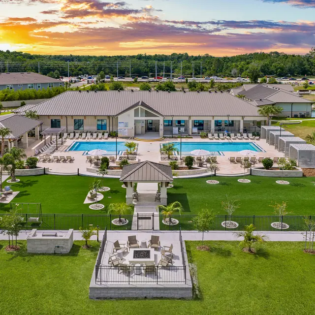 Resort Style Pool Area Aerial view of a resort-style pool area featuring a modern building with a swimming pool surrounded by lounge chairs and landscaped gardens. The sunset casts a warm glow over the scene.