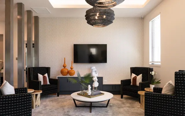 A modern living room with stylish black chairs, a white circular coffee table, a wall-mounted TV, and decorative orange vases on a cabinet.