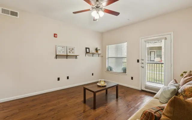 Spacious Living Room Design A well-lit living room with hardwood flooring, a ceiling fan, and minimalistic decor featuring a small table and a couch.