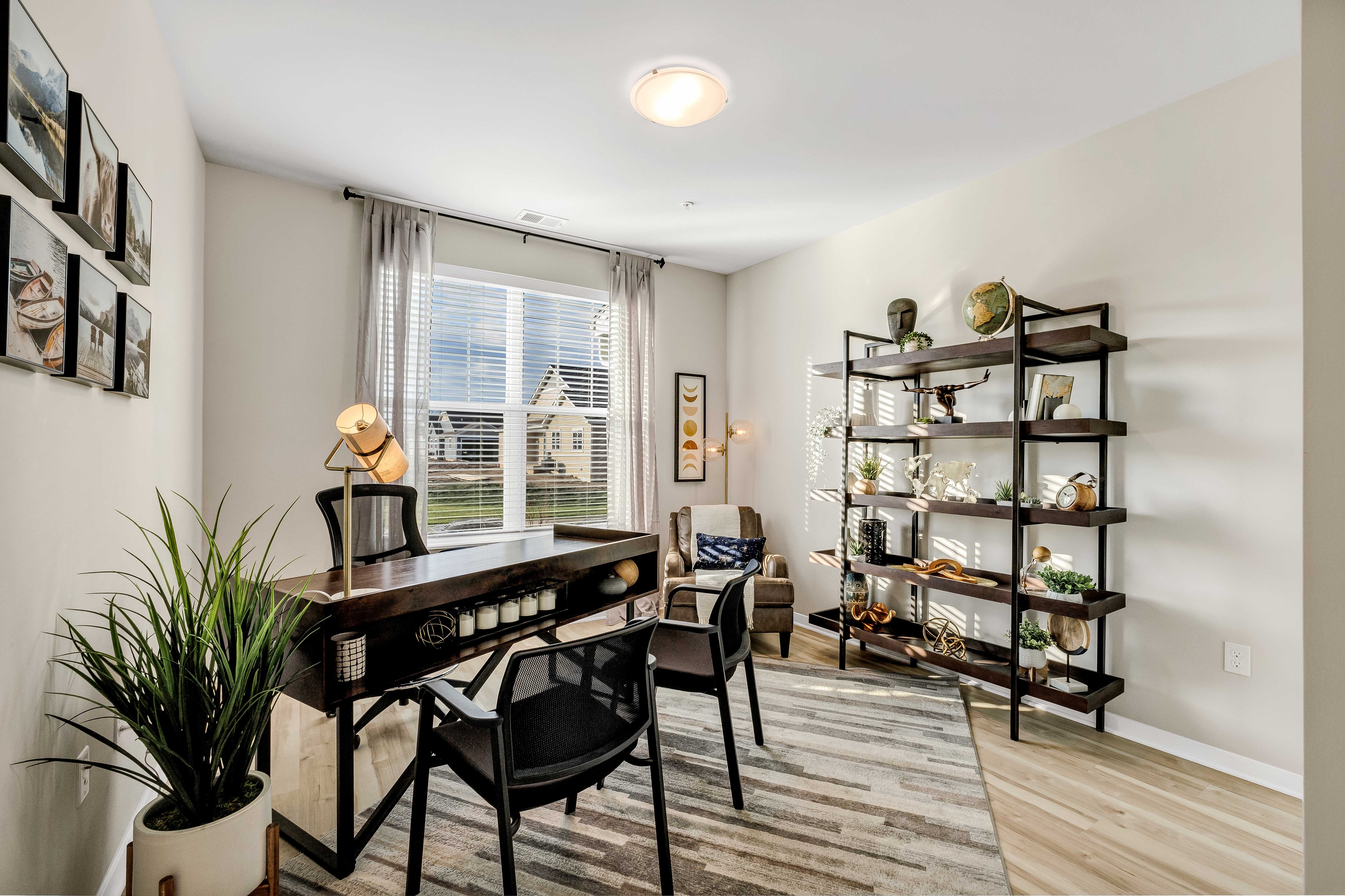 Modern Home Office Interior A modern home office featuring a wooden desk, black chairs, a tall shelving unit decorated with various items, and large windows with curtains allowing natural light to enter.