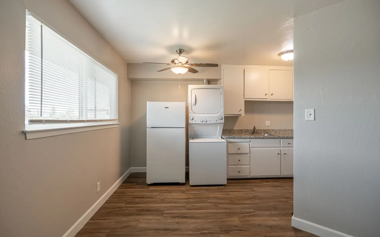 Bright and clean kitchen space featuring a refrigerator, stacked washer and dryer, and light-colored cabinetry against a wooden floor.