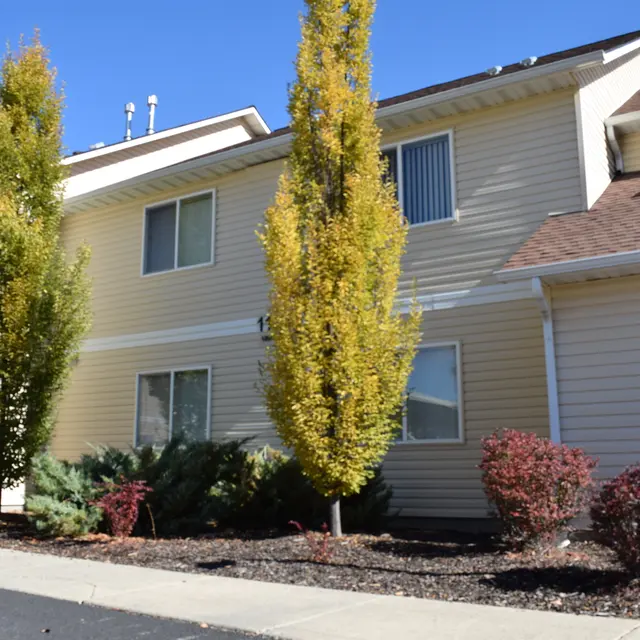 Apartment Building with Landscaping Exterior view of an apartment building with manicured landscaping, featuring tall trees and decorative shrubs.
