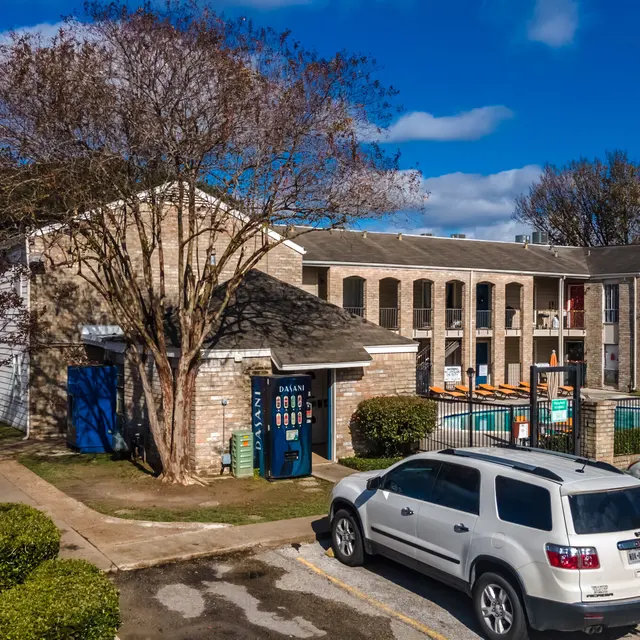 Exterior view of an apartment complex featuring two buildings, one with a pool area and landscaped surroundings.