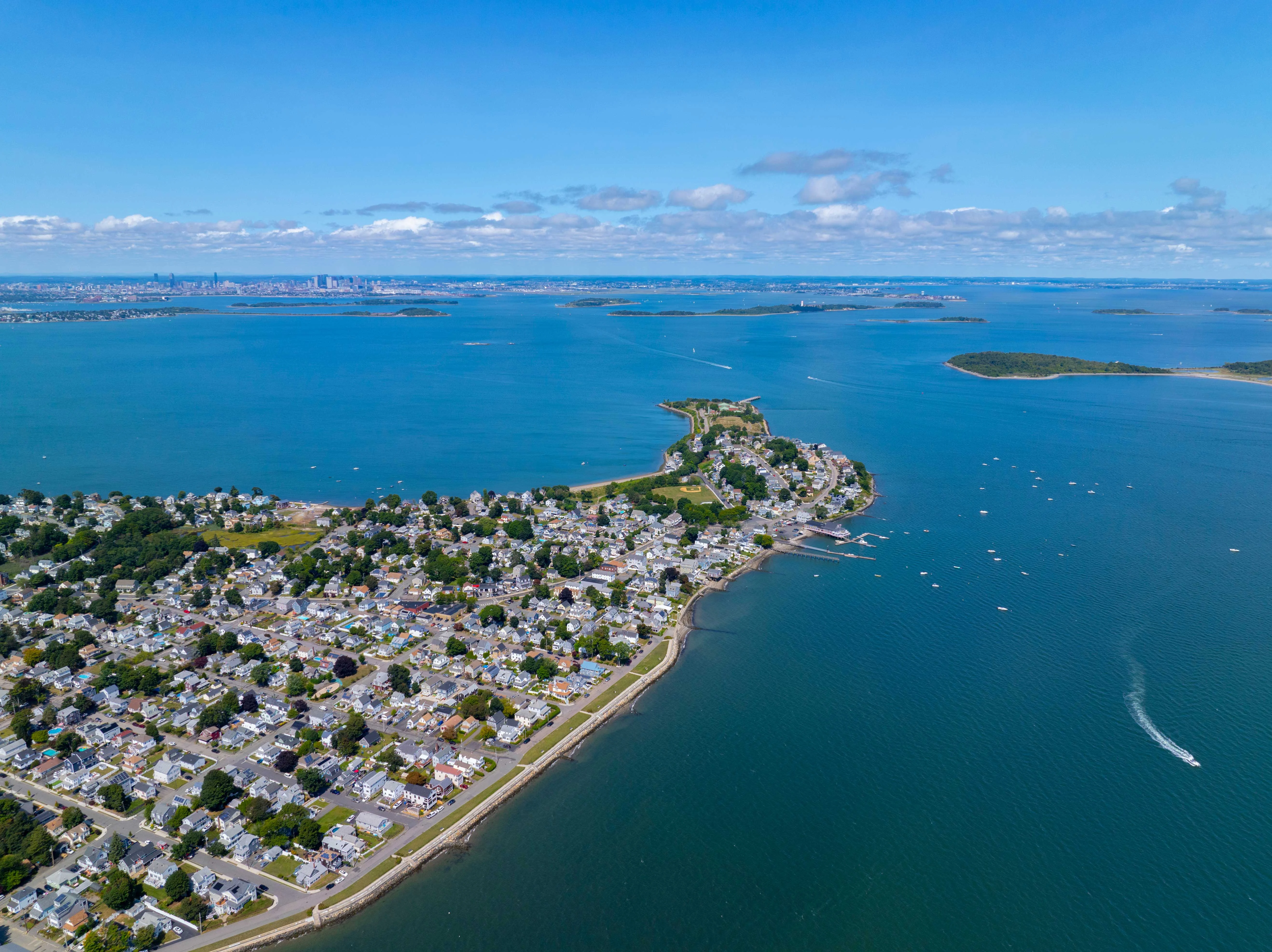 Aerial view of a coastal town with houses along the waterfront and boats in the water under a clear blue sky.