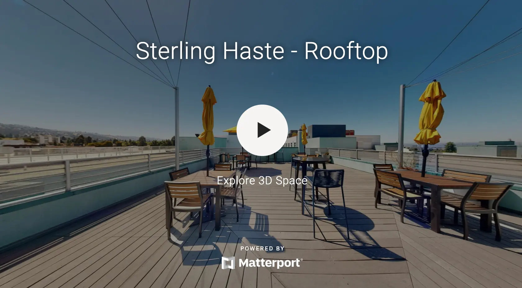 Rooftop area of Sterling Haste featuring wooden furniture and yellow umbrellas against a clear blue sky.