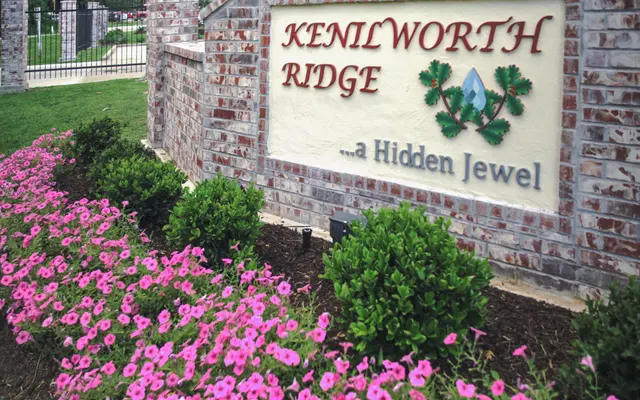 A sign that reads 'KENILWORTH RIDGE ...a Hidden Jewel' surrounded by pink flowers and green shrubs.