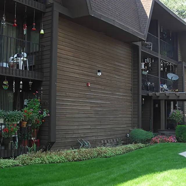 Exterior view of a two-story apartment building with wooden siding and balconies adorned with flower pots and decorative items.
