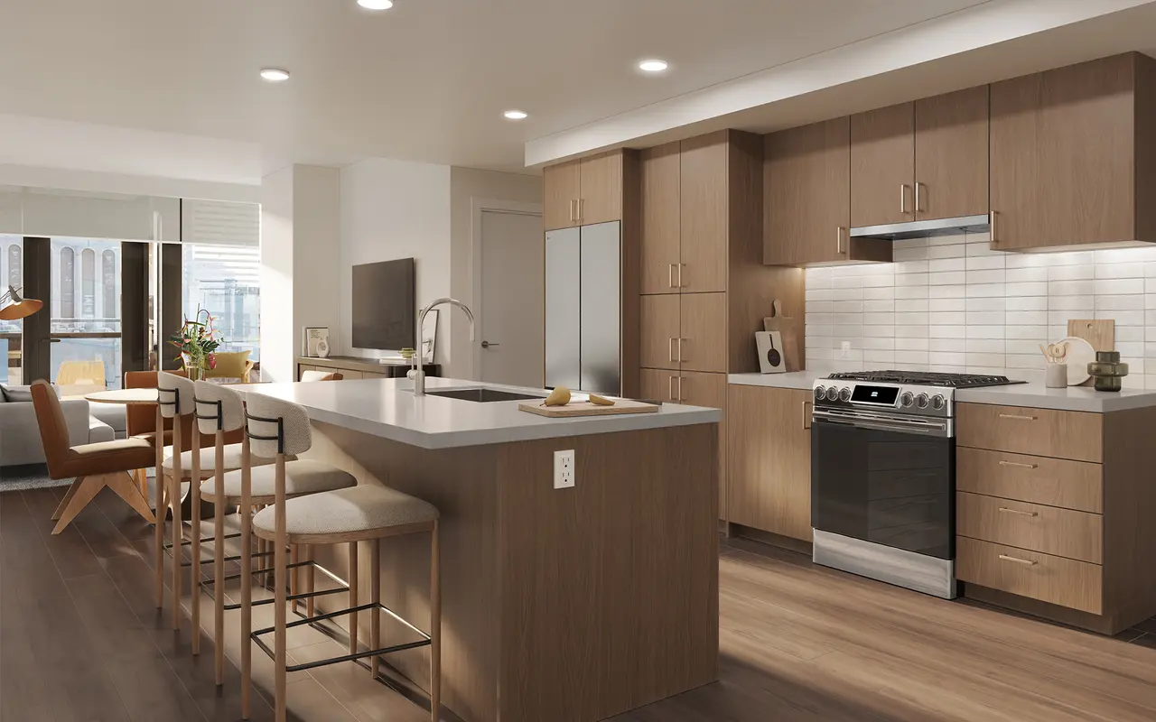 A modern kitchen featuring wooden cabinetry, stainless steel appliances, and a large island with barstools beneath recessed lighting. Natural light flows in through large windows.
