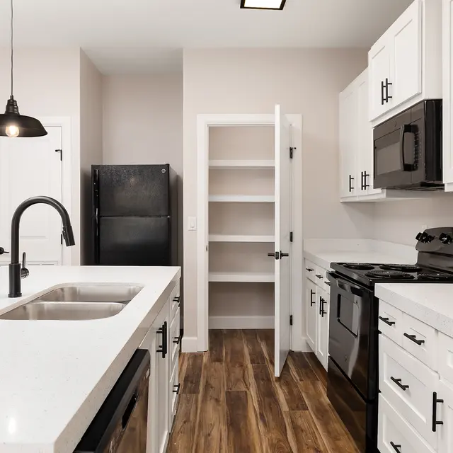 A modern kitchen featuring white cabinetry and stainless steel appliances, with a large island and dark wood flooring.