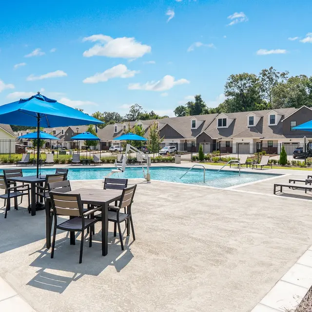 Community Pool Area A vibrant pool area in a community setting, featuring blue umbrellas and lounge chairs around a clear pool on a sunny day.