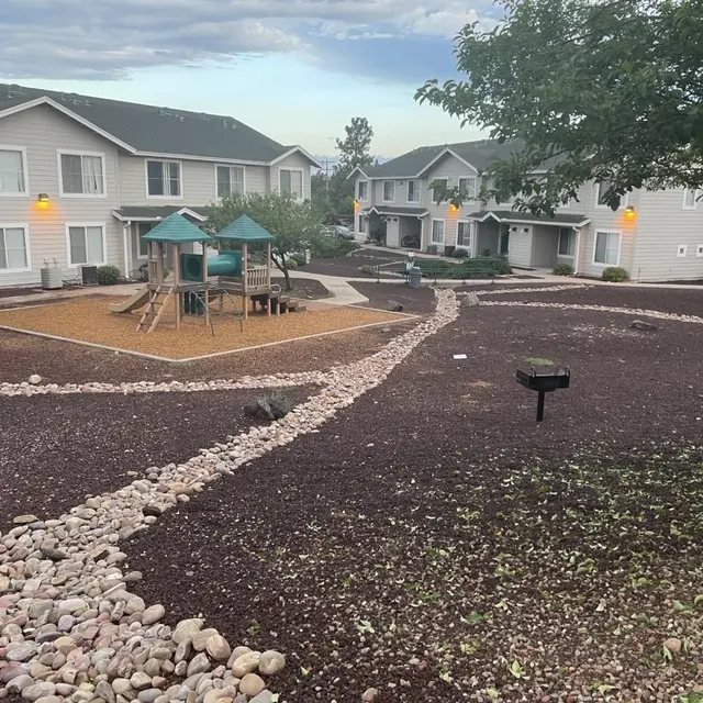 Apartment Complex Courtyard with Playground A view of an apartment complex courtyard featuring a playground with a slide and swings, surrounded by landscaped gravel pathways and scattered rocks, showing a pleasant environment for residents.