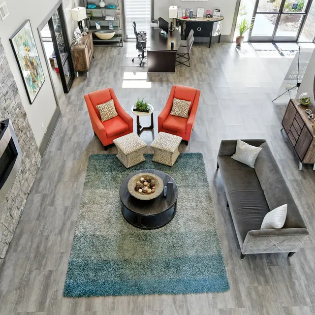 An overview of a modern living room with a stone wall, a fireplace, red armchairs, a grey couch, and a centerpiece table on a patterned rug.
