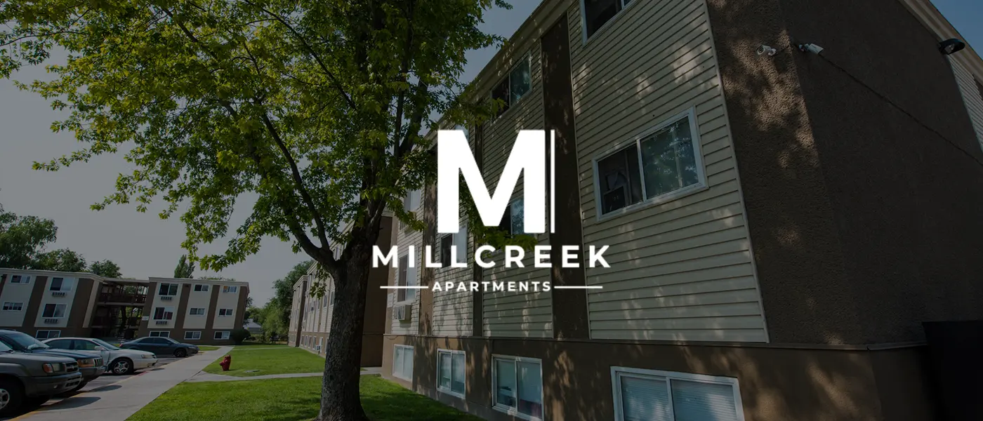 Exterior view of Millcreek Apartments with trees and parked cars