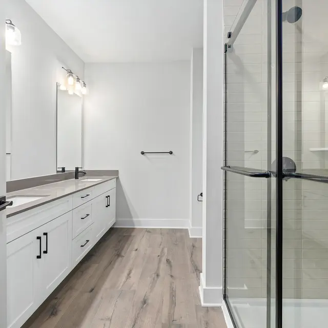 Stylish Modern Bathroom Interior A spacious modern bathroom featuring a large vanity with dual sinks, illuminated mirrors, and a glass shower enclosure. The flooring is light wood, contributing to a bright and airy feel.