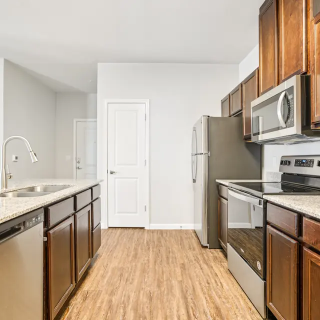 A modern kitchen featuring granite countertops, wooden cabinets, and stainless steel appliances, with a focus on an island and open layout.