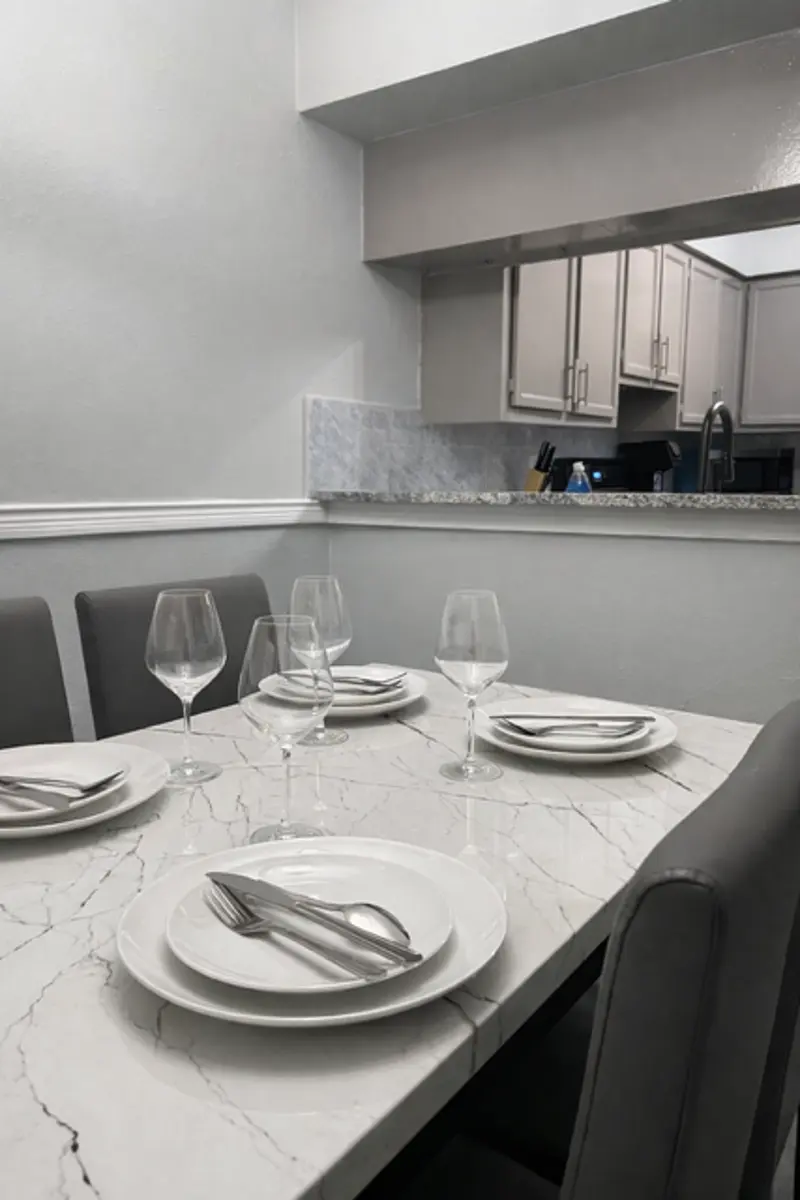 A modern dining table set with plates and wine glasses, featuring a marble surface and grey chairs, in a well-lit kitchen environment.