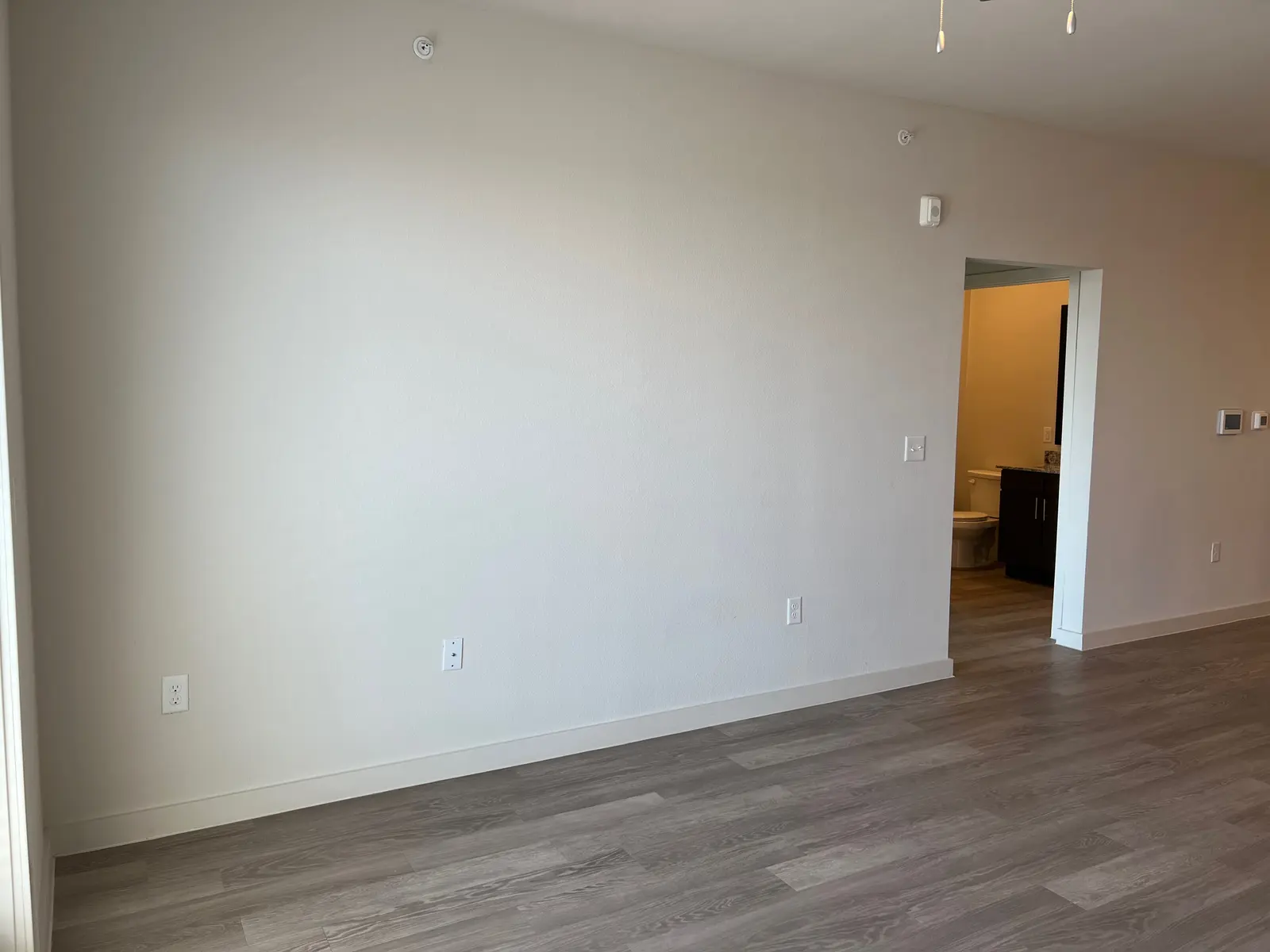 An empty living space with light-colored walls and wooden flooring.