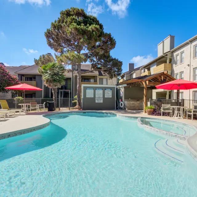 Swimming pool area at an apartment complex with lounge chairs and shaded umbrellas