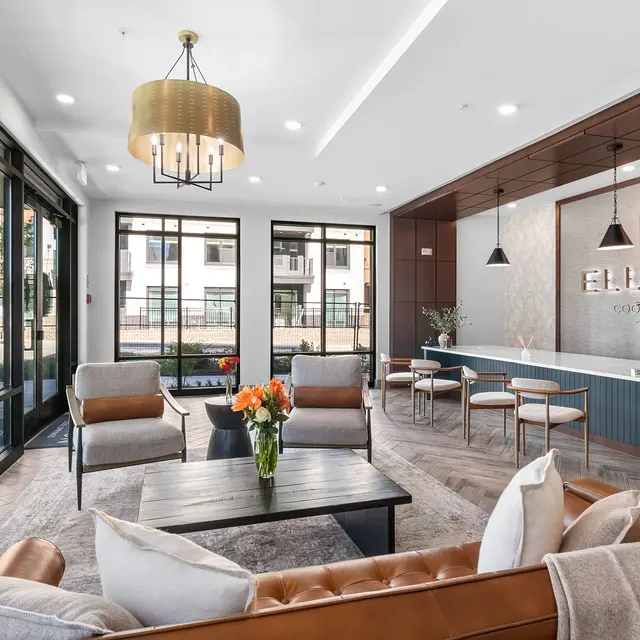 A beautifully designed lobby featuring contemporary furniture, large windows, and bright decor. There are couches and chairs arranged around a coffee table with a vase of flowers. The room has a welcoming and stylish ambiance.