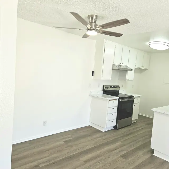A modern kitchen featuring white cabinetry, a black stove, and a silver ceiling fan. The floor is made of light wooden planks, enhancing the bright and airy feel of the space.