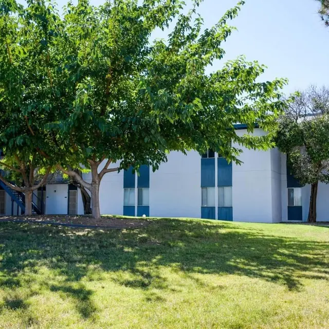 A low-rise apartment complex surrounded by green grass and trees on a sunny day.