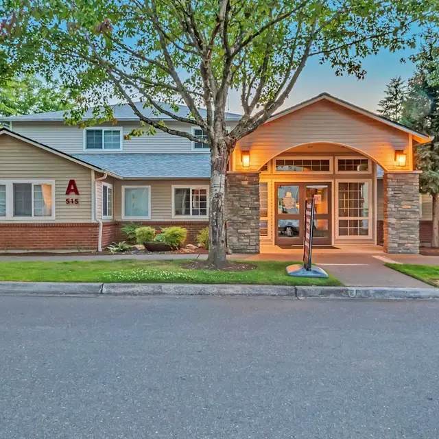 A residential building with a welcoming entrance, surrounded by trees and grass, located on a suburban street.