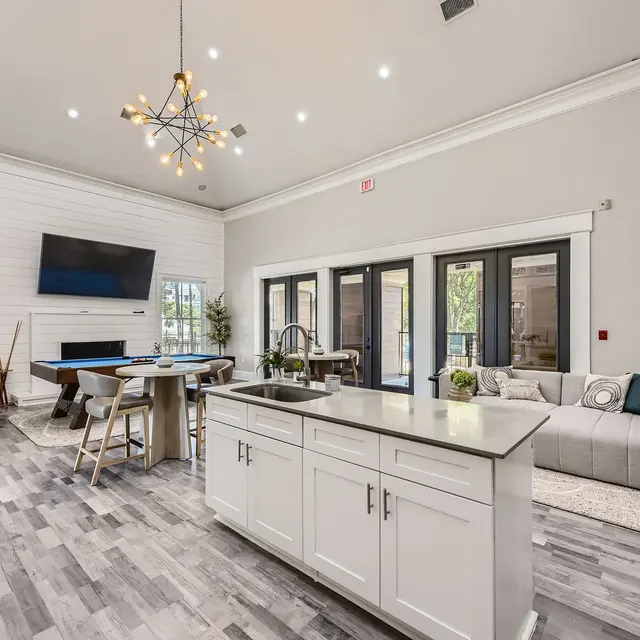 A spacious, modern living area featuring a kitchen island, dining table, and comfortable seating arrangement with large windows leading to an outdoor space.