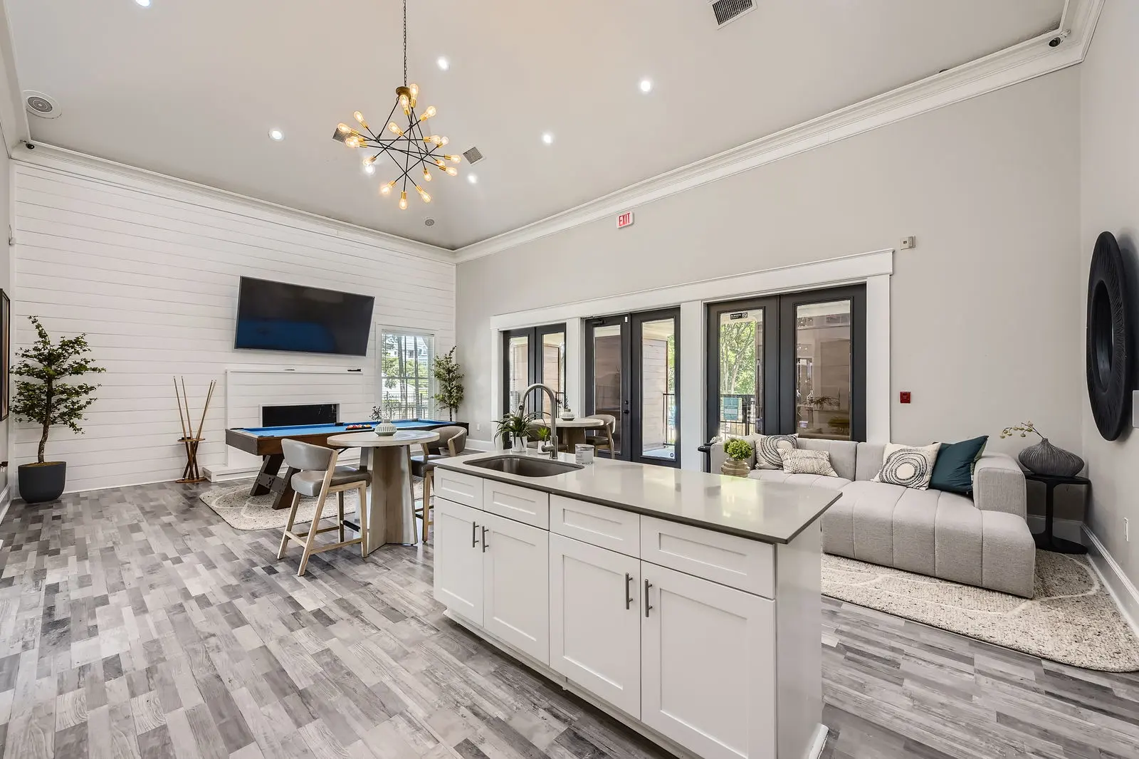 A spacious, modern living area featuring a kitchen island, dining table, and comfortable seating arrangement with large windows leading to an outdoor space.