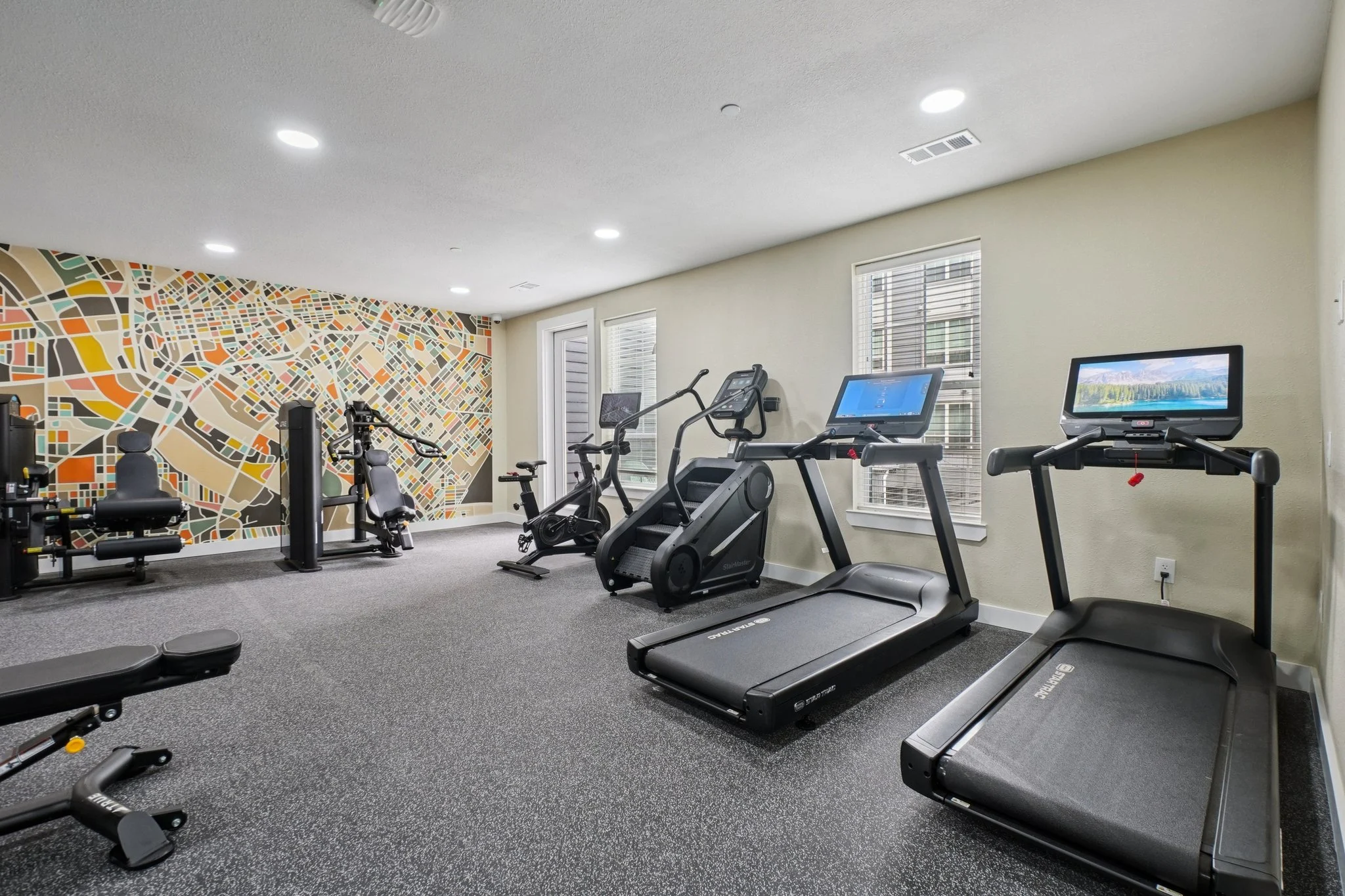 Modern Fitness Center A modern gym featuring various exercise equipment, including treadmills, ellipticals, and weight machines, with a colorful map-themed wall.