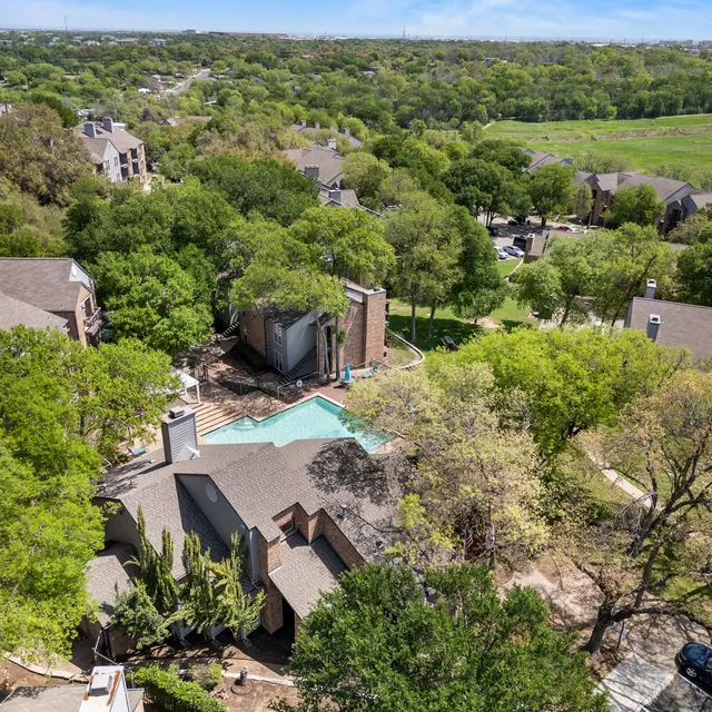 Aerial view of an apartment complex surrounded by greenery and trees, featuring a swimming pool in the center.