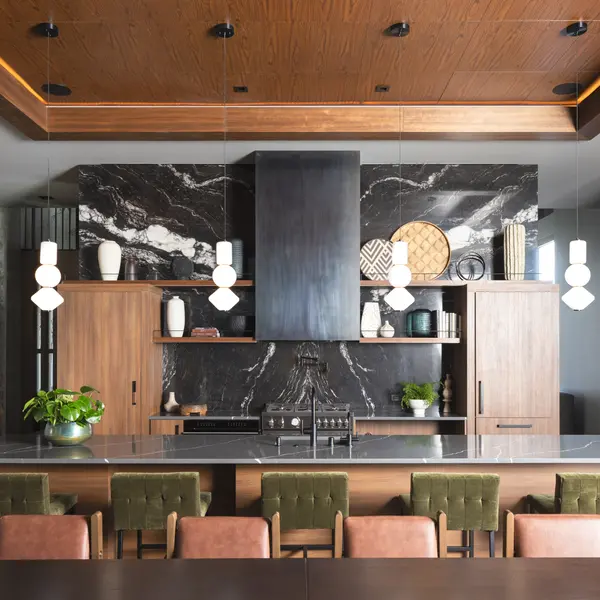 A contemporary kitchen with a large island, wooden cabinets, a dark marble backsplash, modern light fixtures, and a dining area.