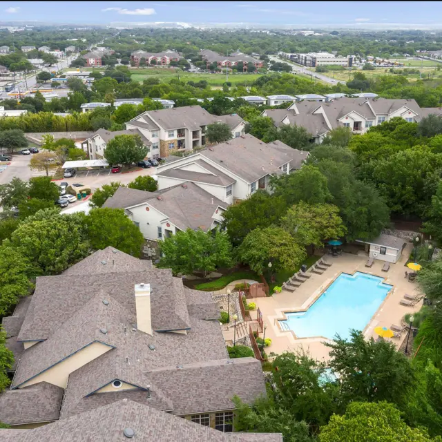 Aerial view of an apartment complex featuring a swimming pool surrounded by greenery.