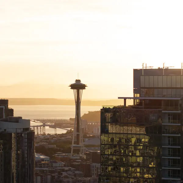 A scenic view of Seattle's skyline at sunset, featuring the Space Needle and multiple modern buildings reflecting sunlight.