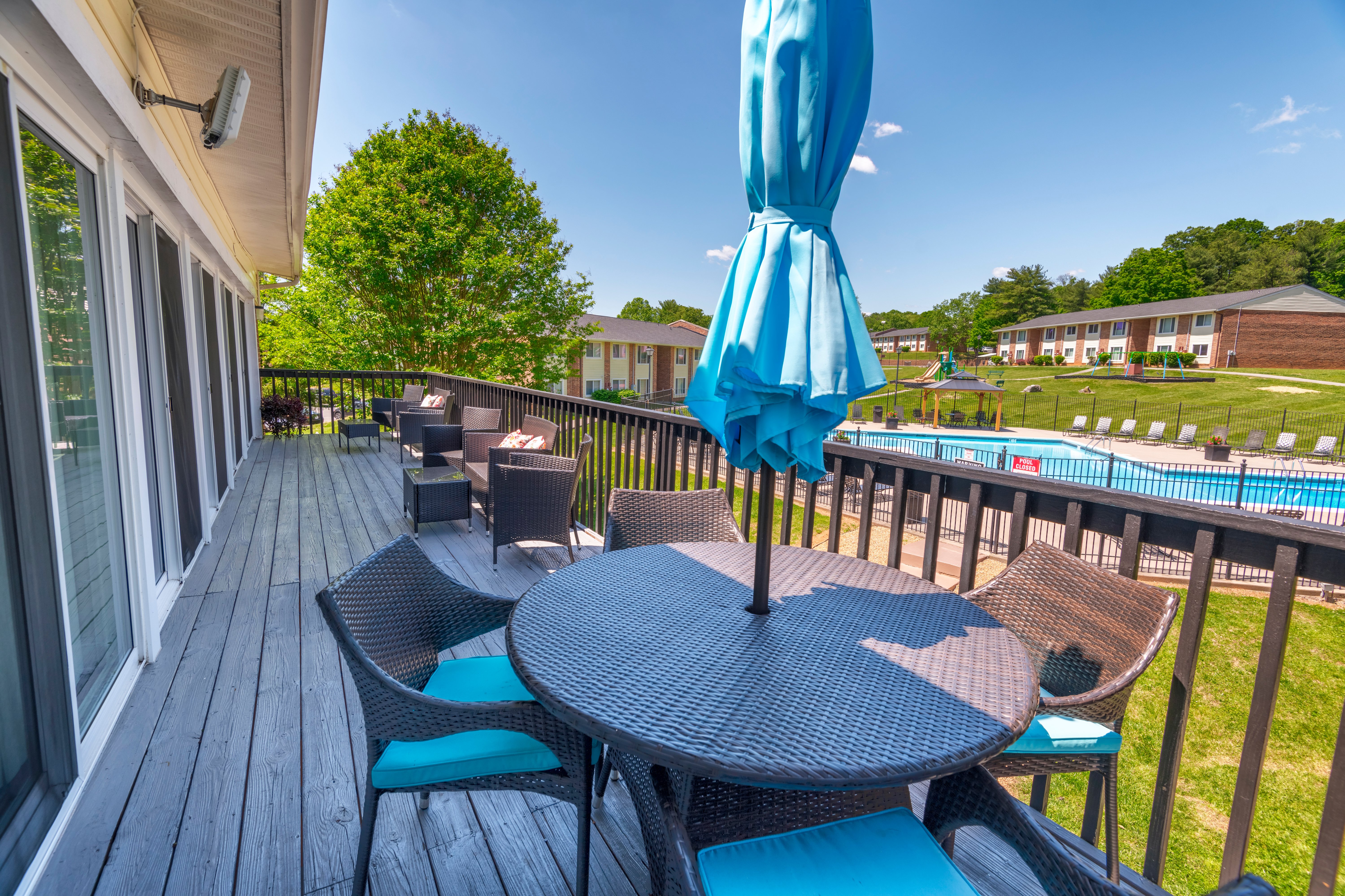 A spacious balcony with outdoor furniture overlooking a pool and green areas in the background.