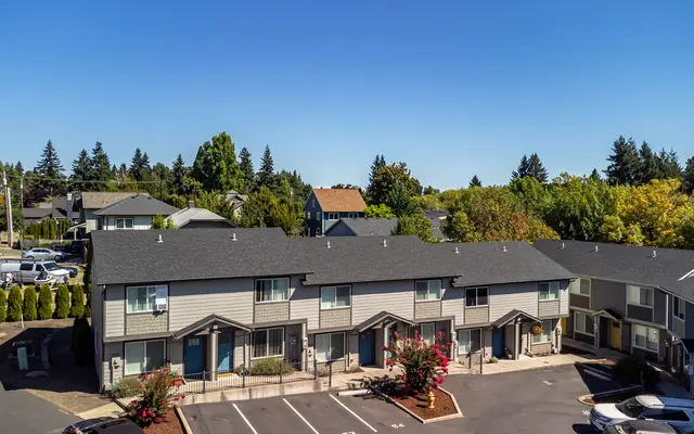 Aerial view of a residential complex featuring multiple two-story townhouses surrounded by green trees and blue skies.