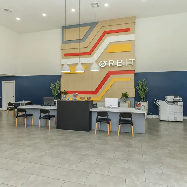 A modern reception area with a high ceiling, featuring a colorful wall with the word 'ORBIT' and stylish furniture.