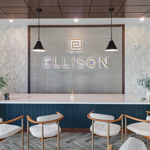 Modern reception area featuring a sleek counter with the name 'ELLISON' illuminated on the wall. Stylish seating and decor elements enhance the ambiance.