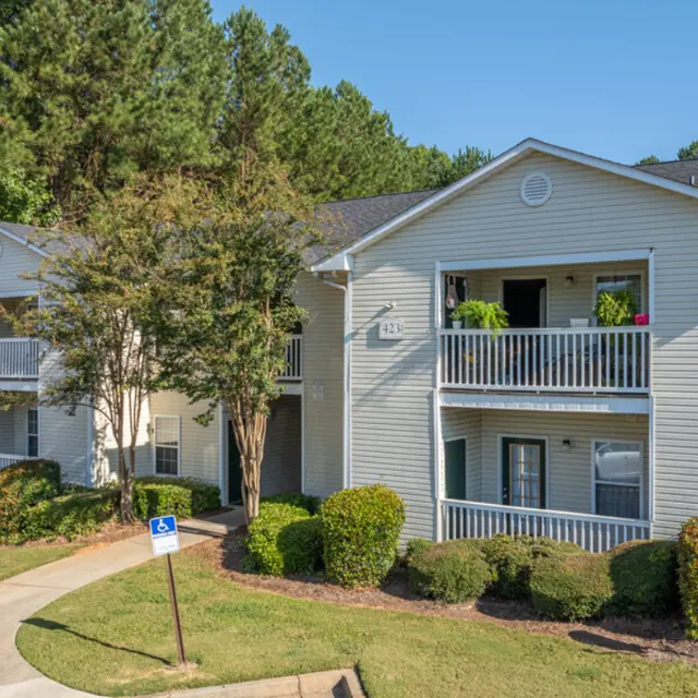 Exterior view of two-story apartment building surrounded by greenery, featuring balconies and a well-maintained landscape.