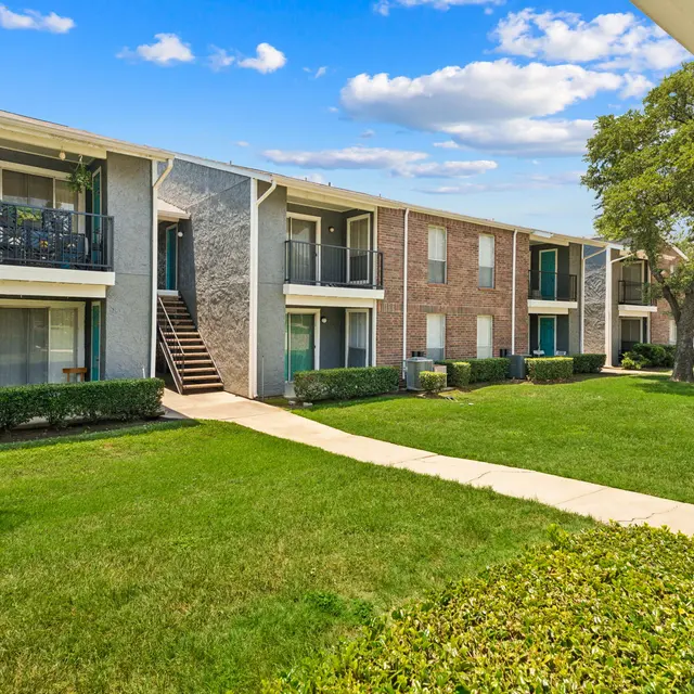 Exterior view of a multi-unit apartment complex with green lawn and trees.
