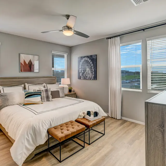 Modern bedroom featuring a bed with white linens, two nightstands, a wooden dresser, and large windows with natural light.