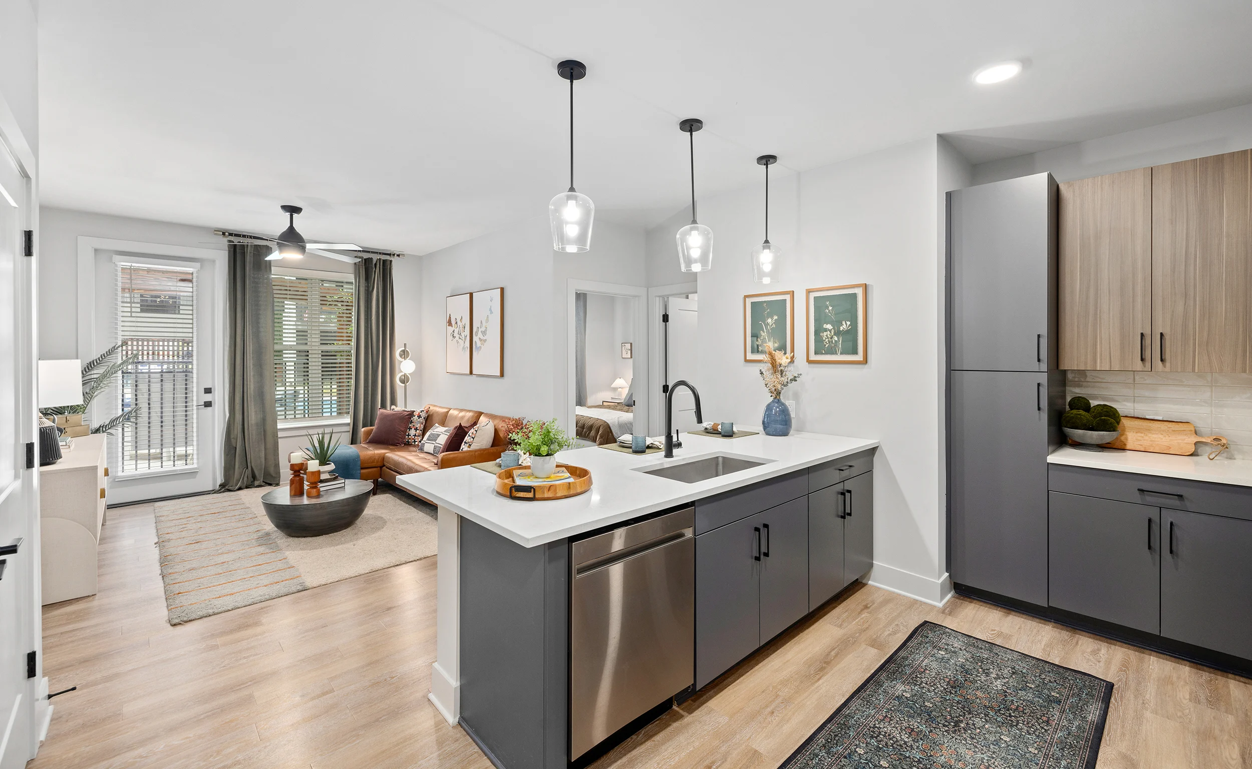 A modern kitchen area with an open layout that connects to a cozy living space. The kitchen features a large island with a stainless steel sink,
