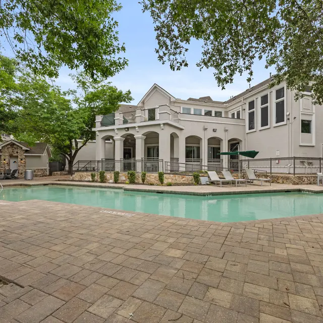 A view of a swimming pool area surrounded by green trees and a modern building.