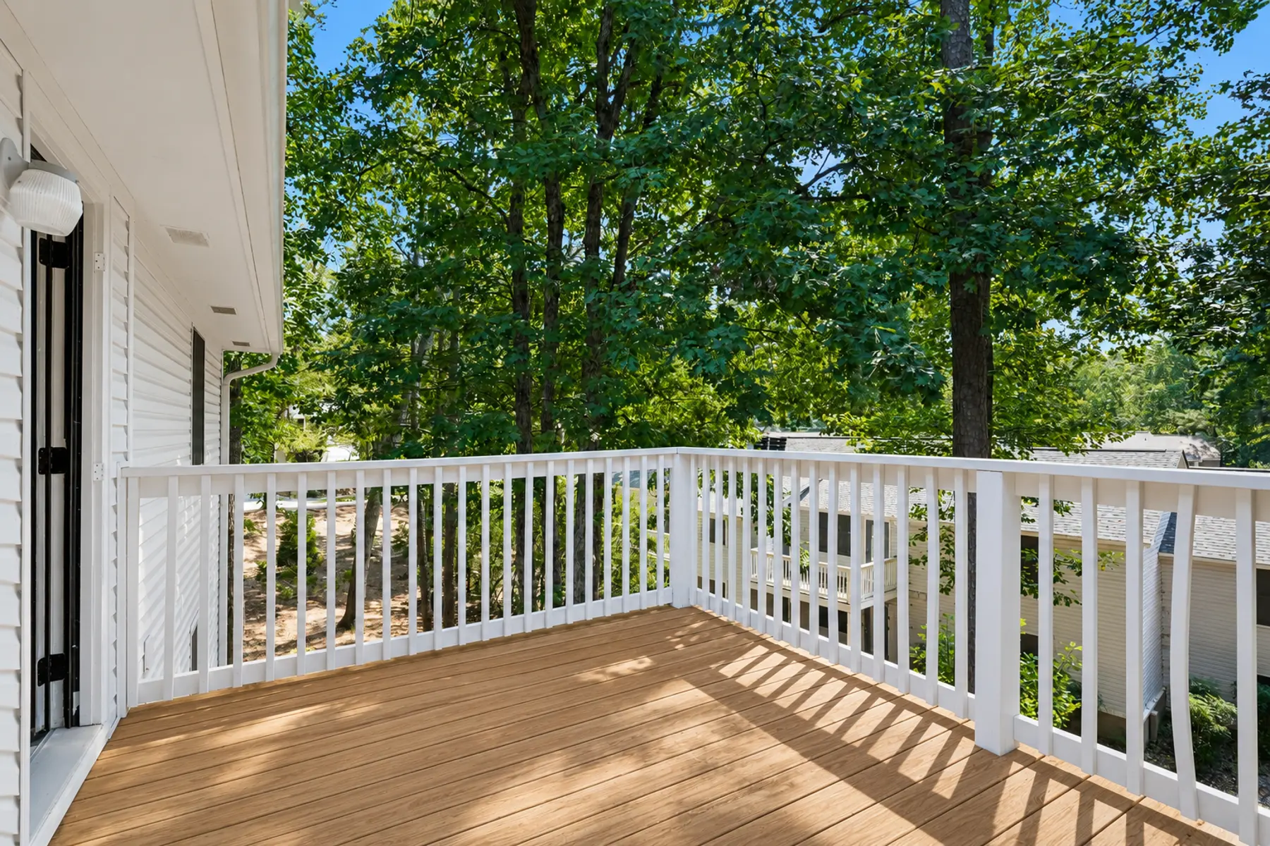 A wooden balcony with a white railing surrounded by green trees.