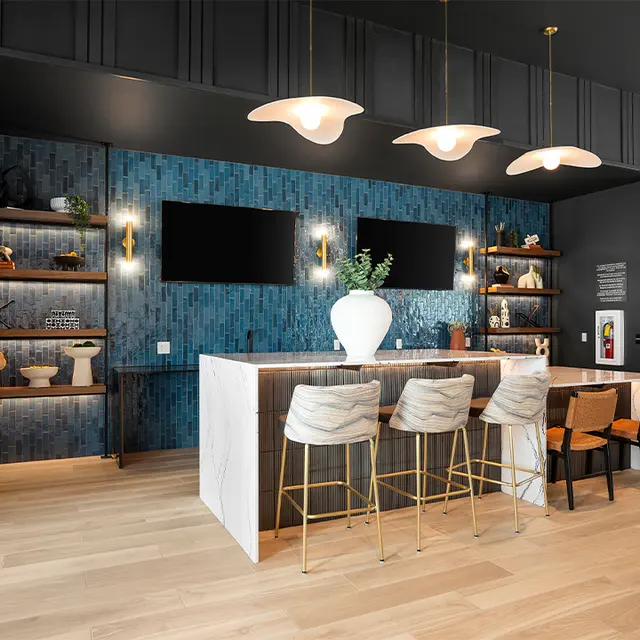 A modern kitchen bar area featuring a white countertop, golden bar stools, blue tiled backdrop, and decorative shelves displaying various items.