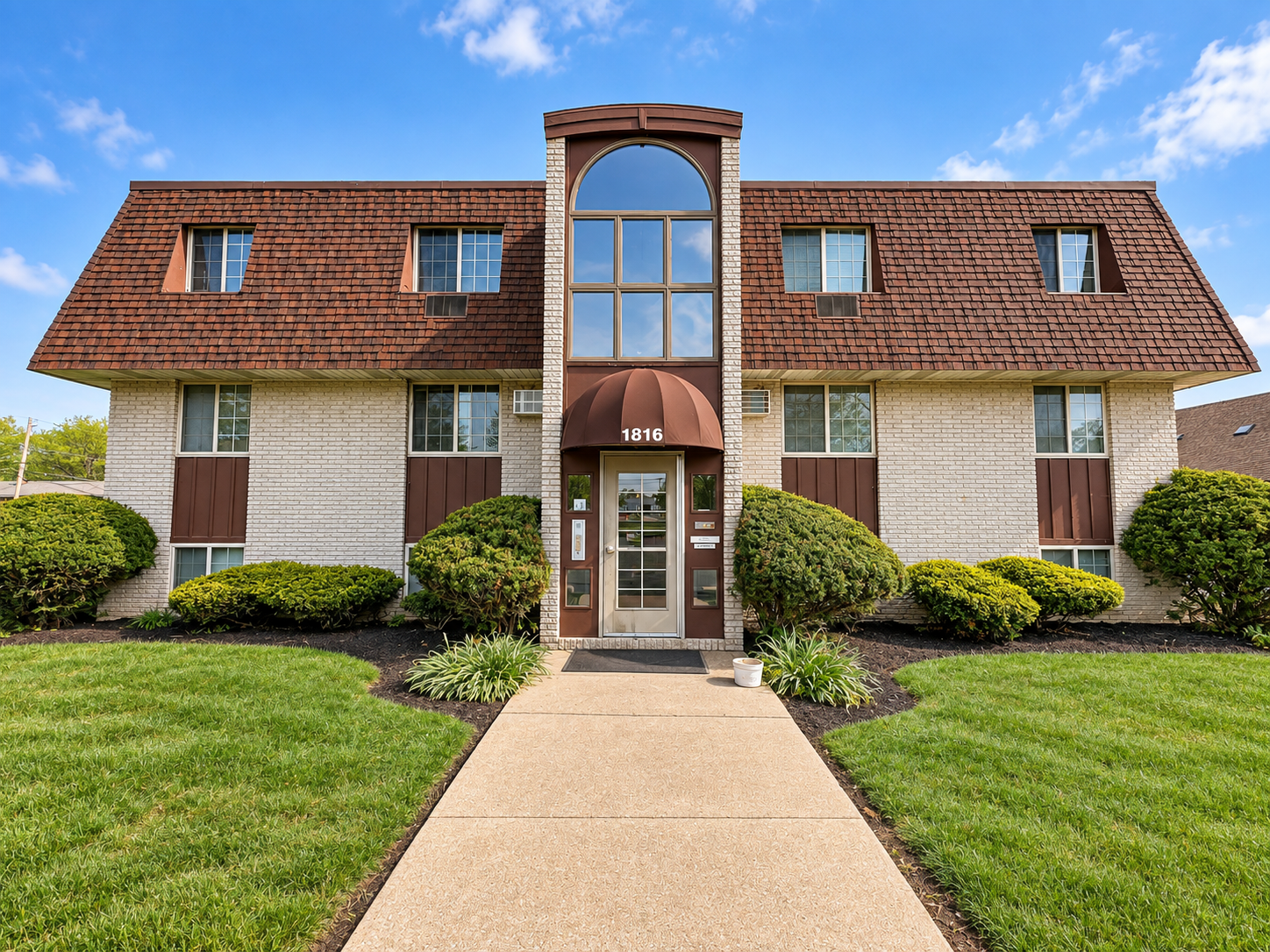 Charming Apartment Building with Distinct Architectural Design Exterior view of a residential apartment building with a central entrance, surrounded by manicured landscaping and a clear blue sky.