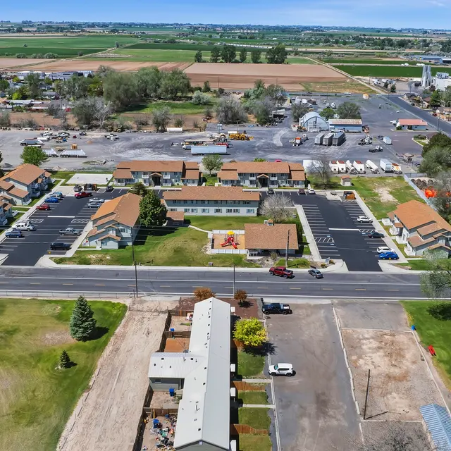 Aerial View of Motel and Surroundings Aerial view of a motel with a parking area, surrounded by green fields and other buildings.